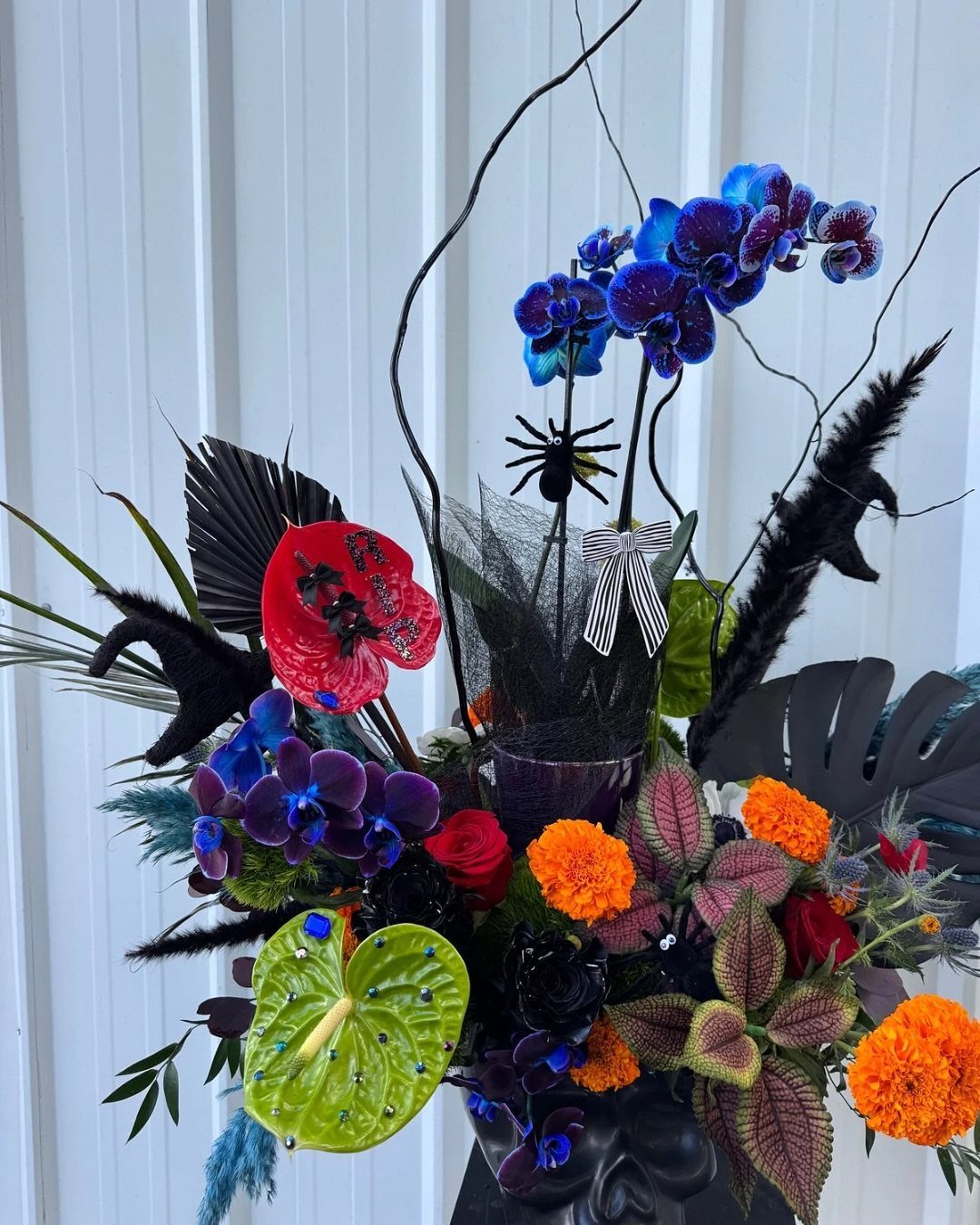 Halloween floral arrangement with blue orchids and orange marigolds in a skull vase.