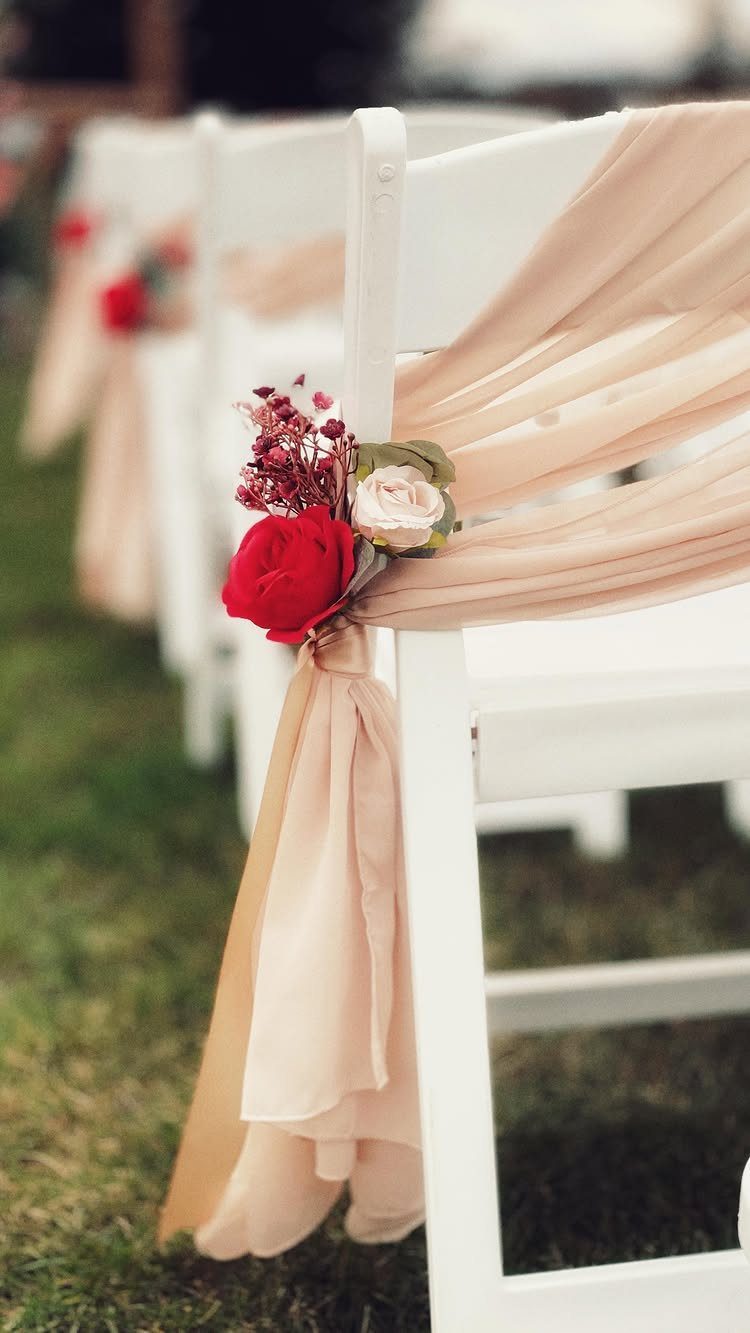 White folding chairs with champagne fabric sashes and red rose floral accents.