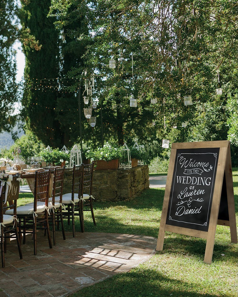 Wooden A-frame chalkboard wedding welcome sign standing on a green lawn outdoors.