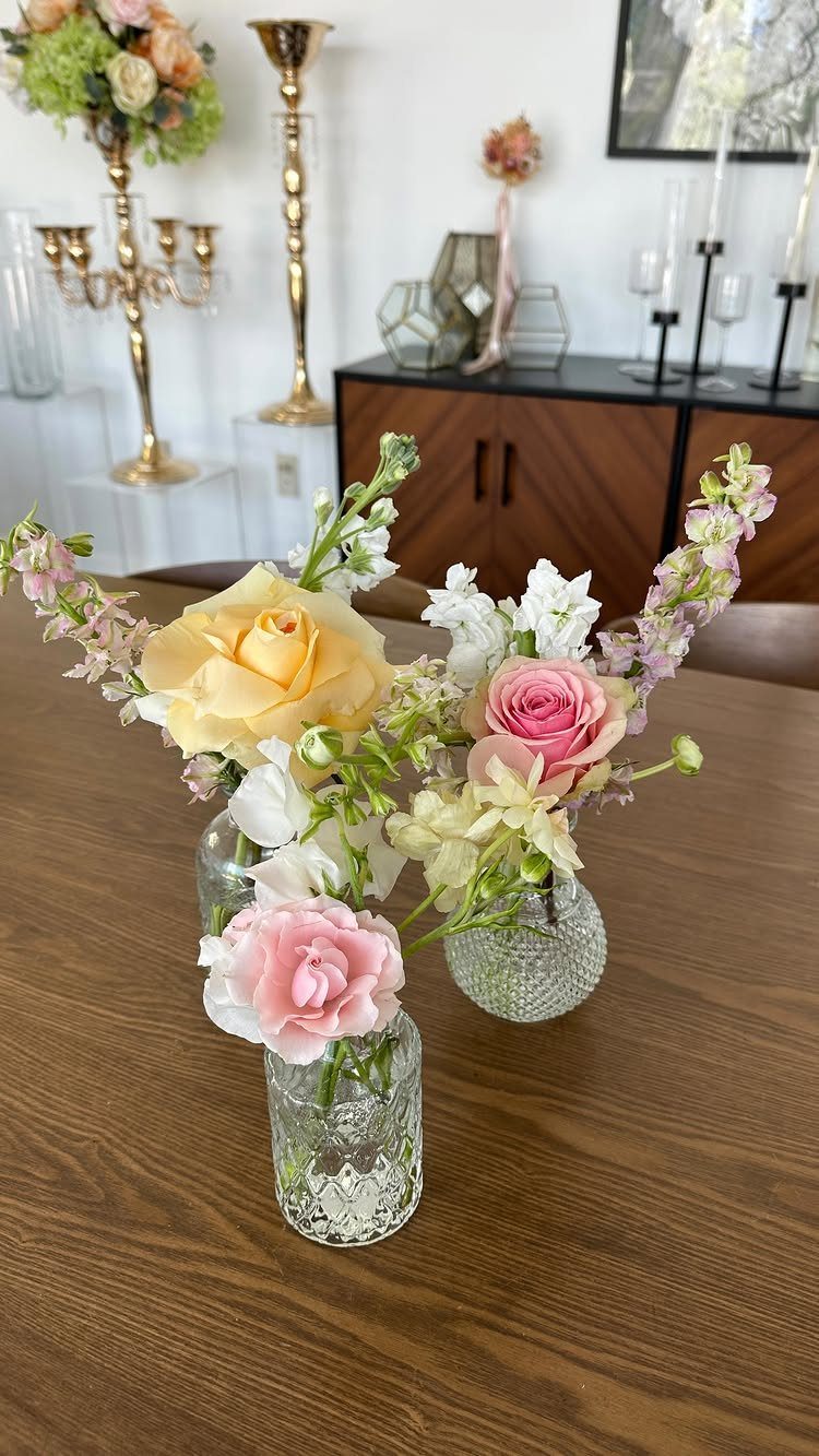 Small glass vases with pink and yellow roses on a wooden table.
