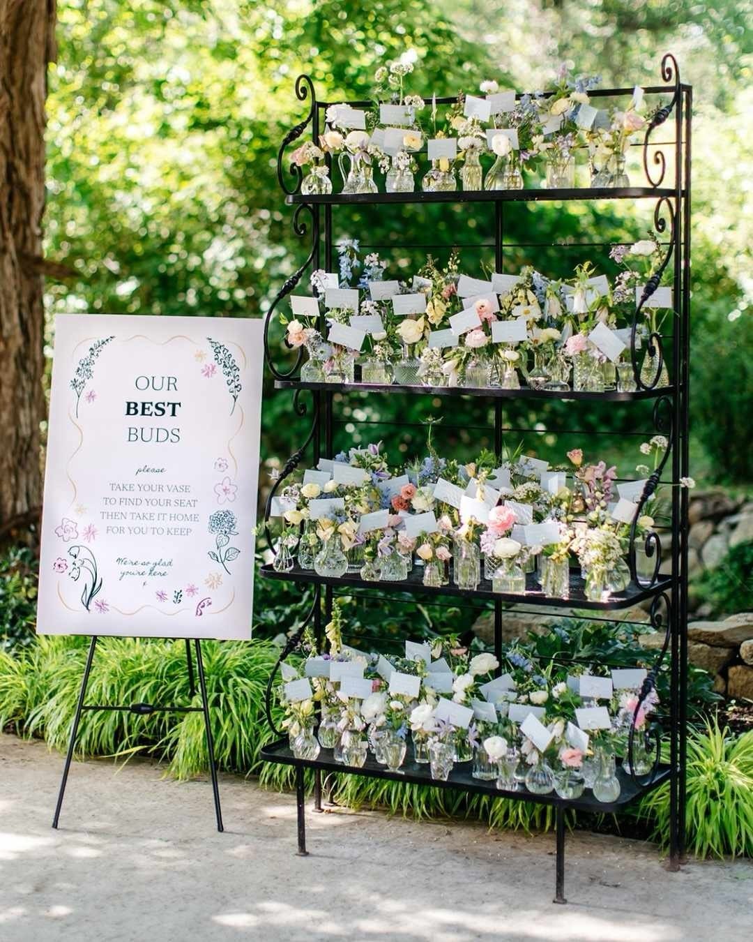 Black metal shelf holding small flower vases and a sign for wedding guests.
