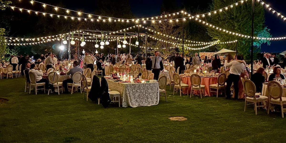 Outdoor wedding reception with warm string lights draped over dining tables on grass