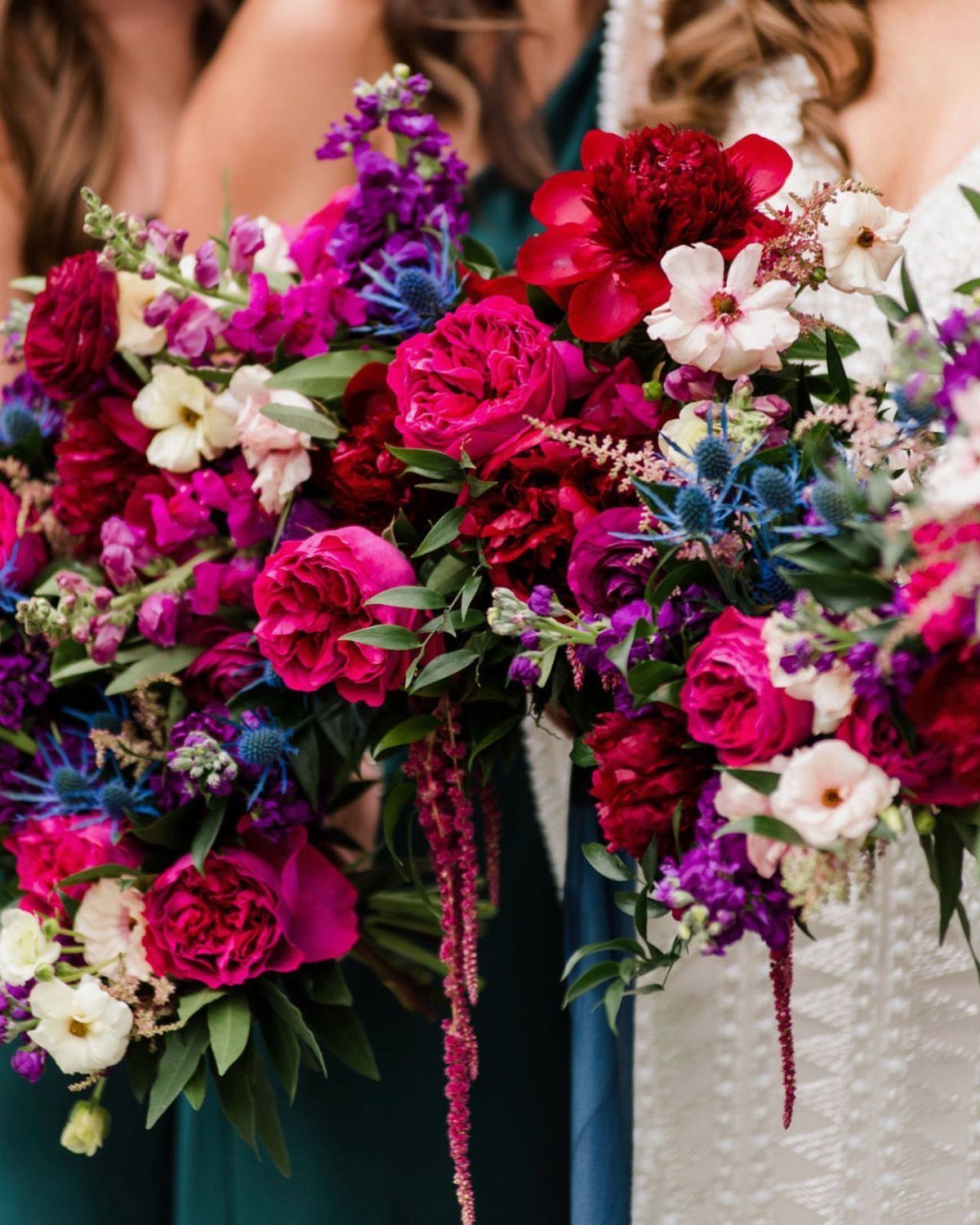 Jewel-toned wedding bouquets with red, magenta, and purple flowers and blue thistles.