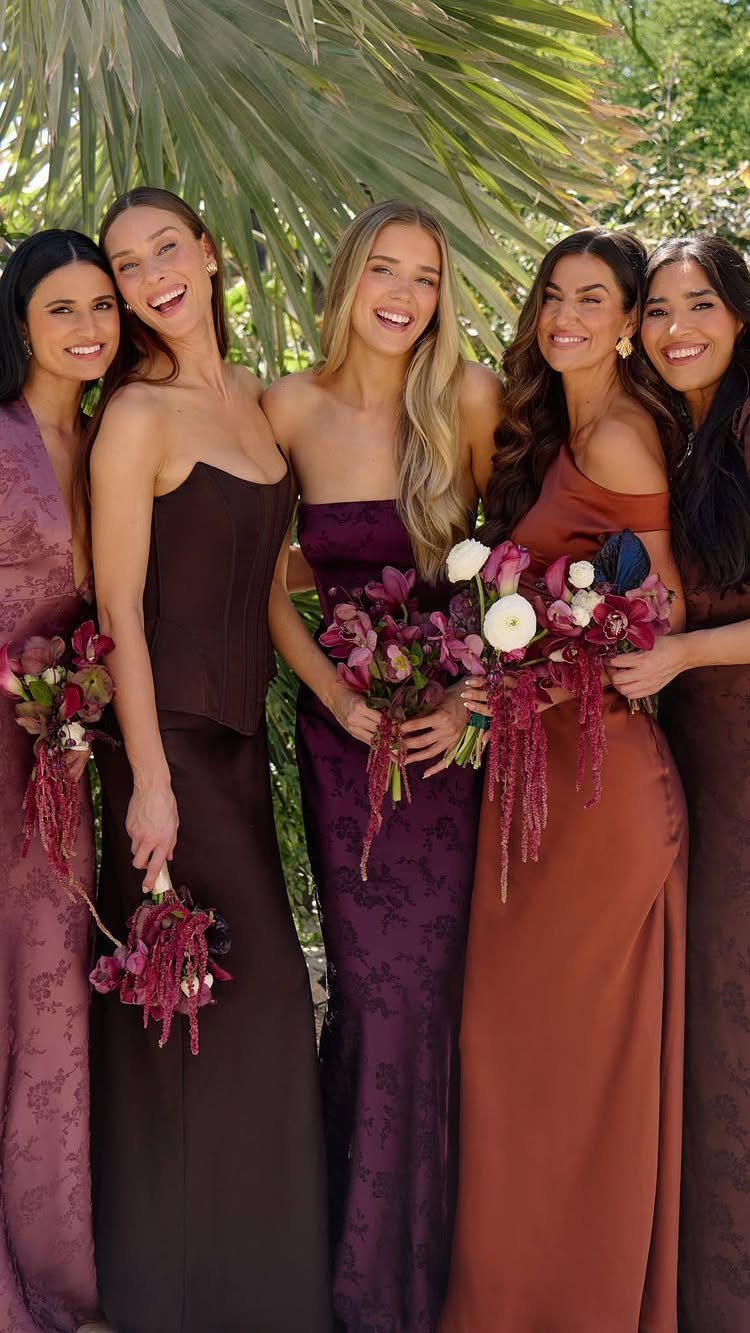Five bridesmaids in mismatched jewel tone dresses holding dark floral bouquets outdoors.