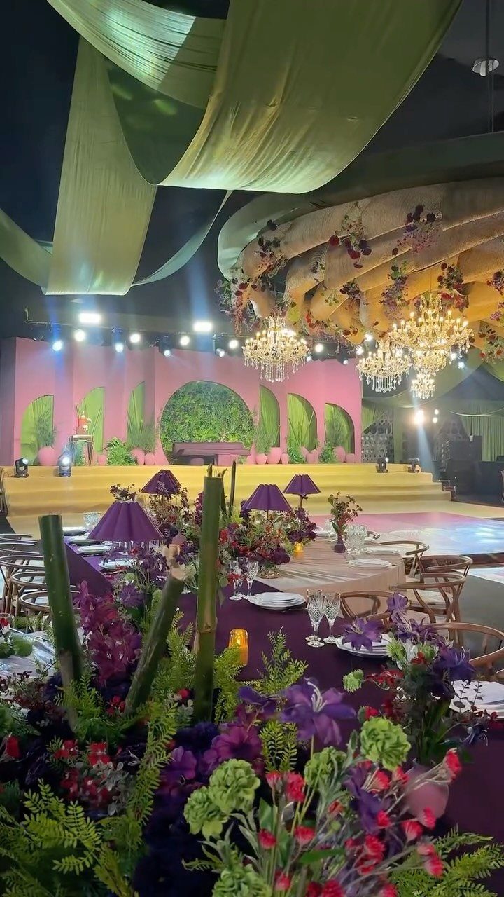 Plum linen tablecloth with purple floral centerpieces under green fabric ceiling drapes.