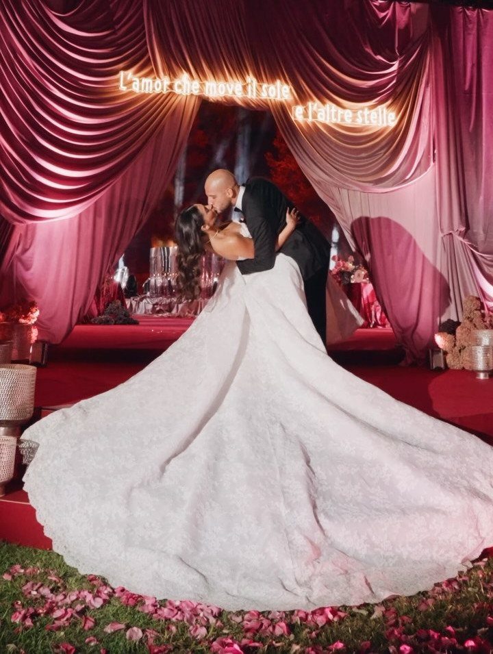 Bride and groom kissing under ruby red draped curtains on a red carpet.