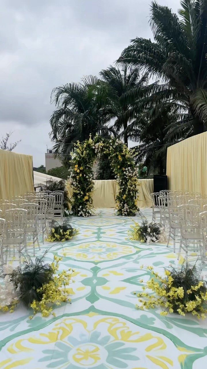 Wedding ceremony aisle with yellow and sage green patterns and a floral arch.