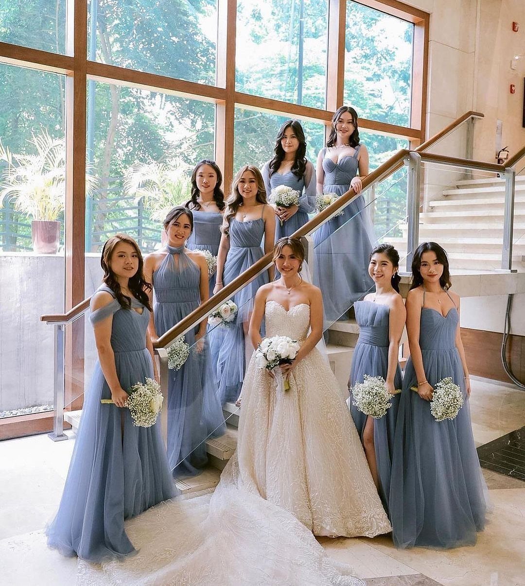 Bride in white gown with bridesmaids in dusty blue dresses on a staircase