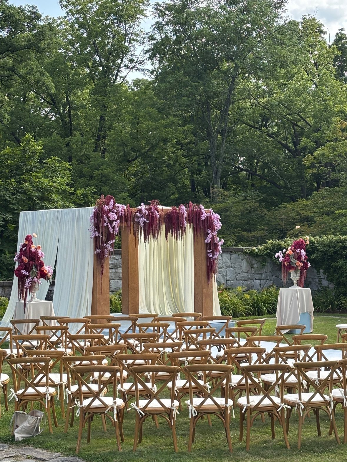 Outdoor wedding ceremony setup with cream fabric and purple floral altar decorations.