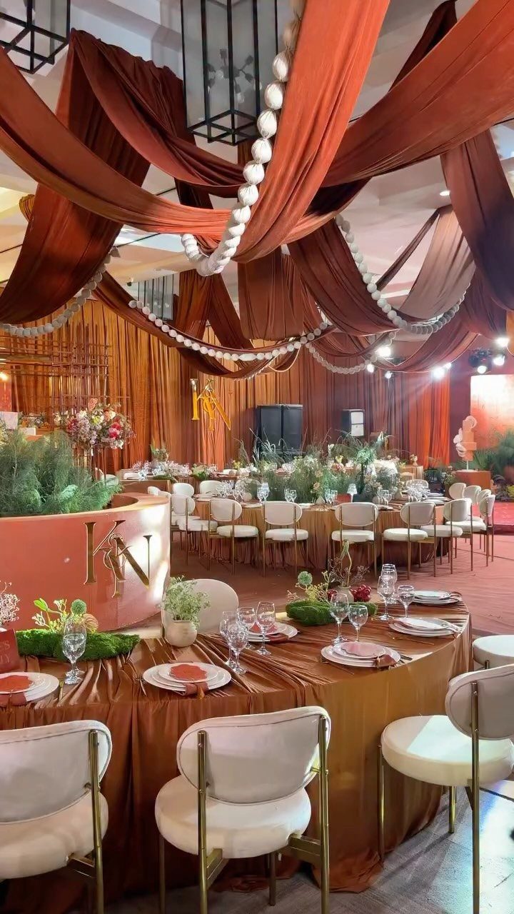 Terracotta fabric ceiling drapes and table linens with white chairs in a ballroom.