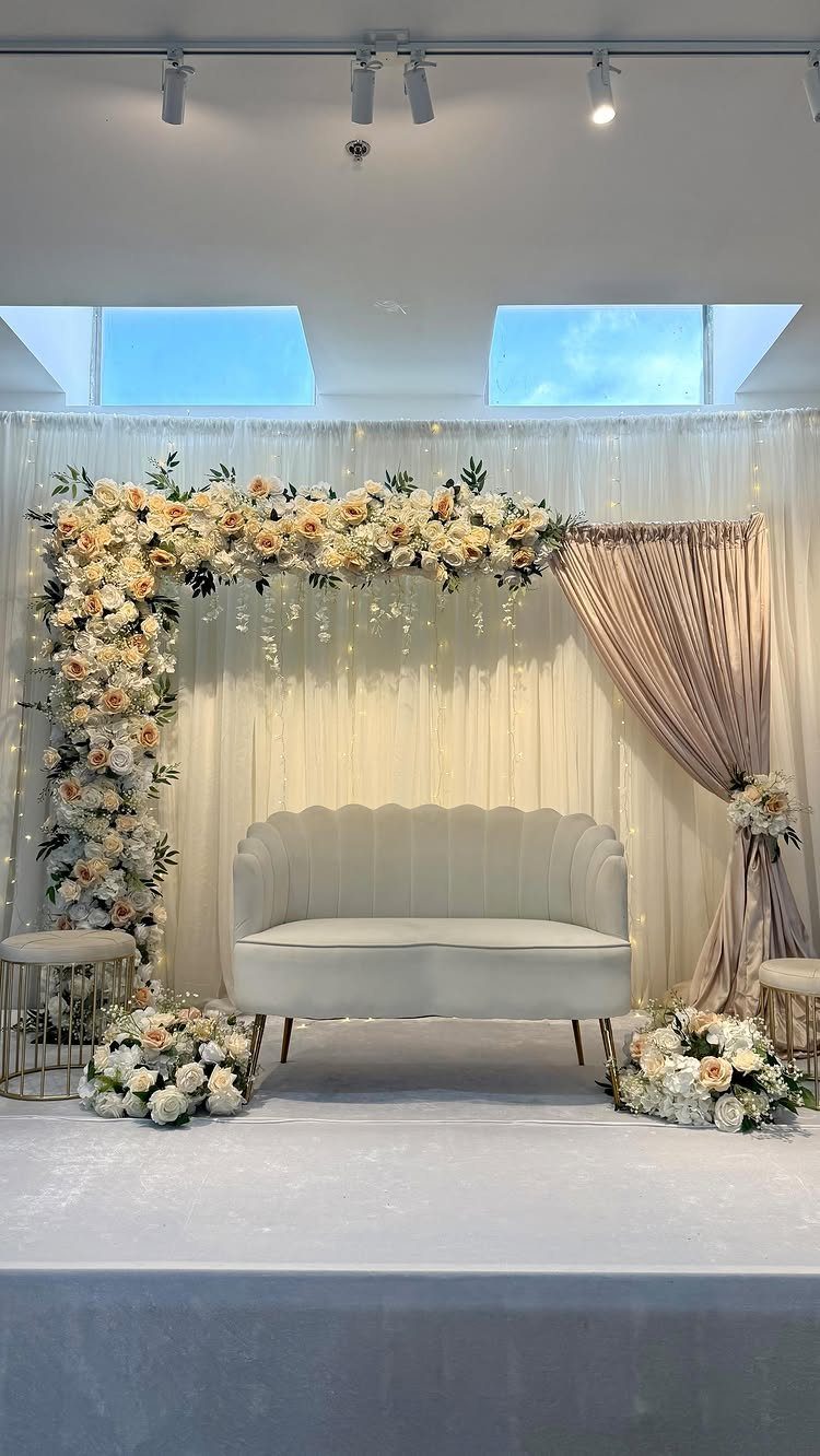 White scalloped sofa on a stage with cream floral arch and beige curtains.
