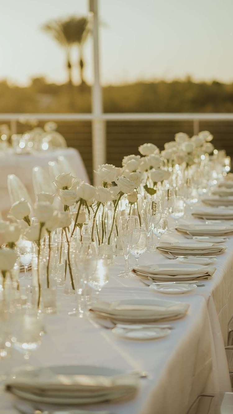 Champagne linens on a wedding table with white flowers and plates outdoors.