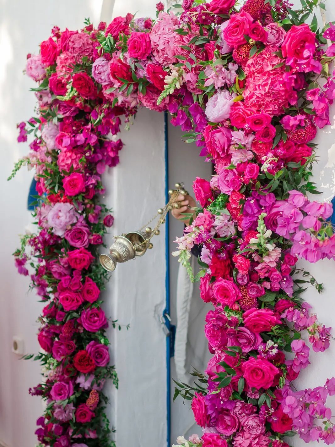 Fuchsia and pink floral arch framing a white doorway with green foliage.