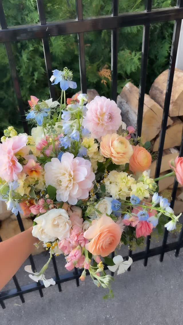 Bridal bouquet with peach, pink, and blue flowers held against a black fence.