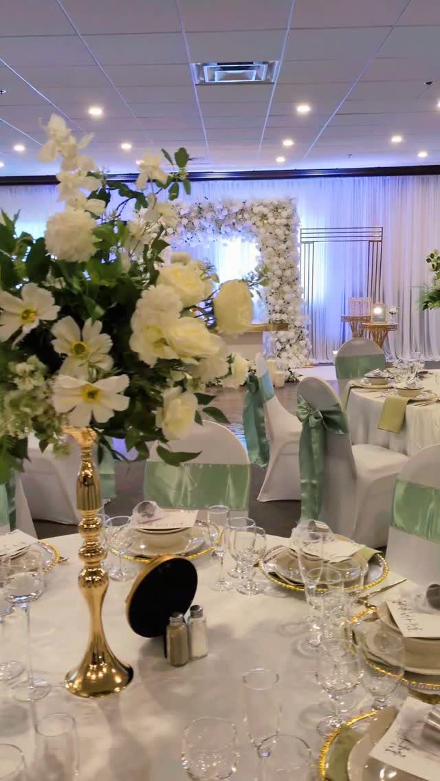 Wedding table setting with white flowers and sage green chair sashes in a hall.