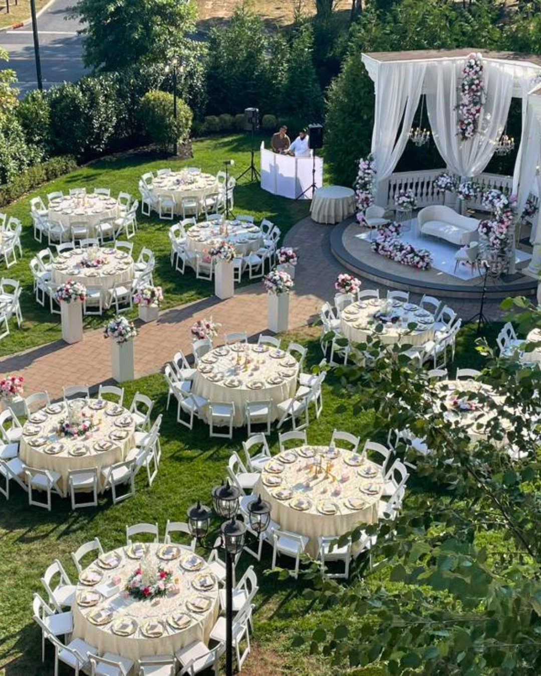 Outdoor wedding reception with cream tables, white chairs, and a draped white gazebo.