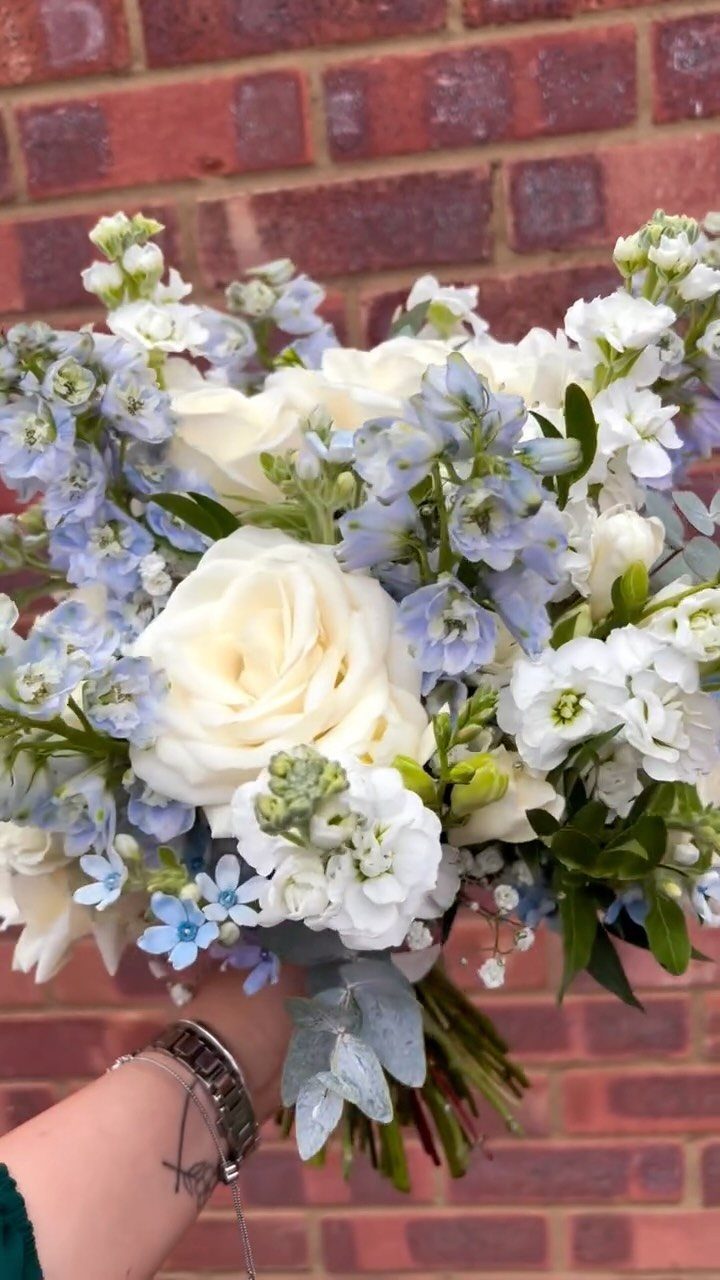Wedding bouquet with white roses and light blue flowers against a brick wall