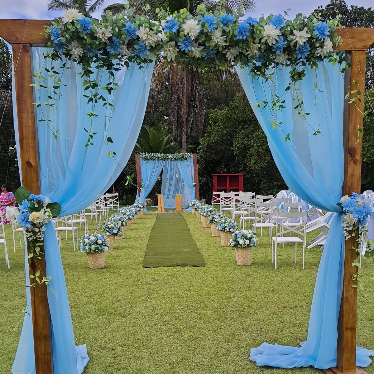 Wooden wedding arch with light blue fabric and blue and white floral arrangements.