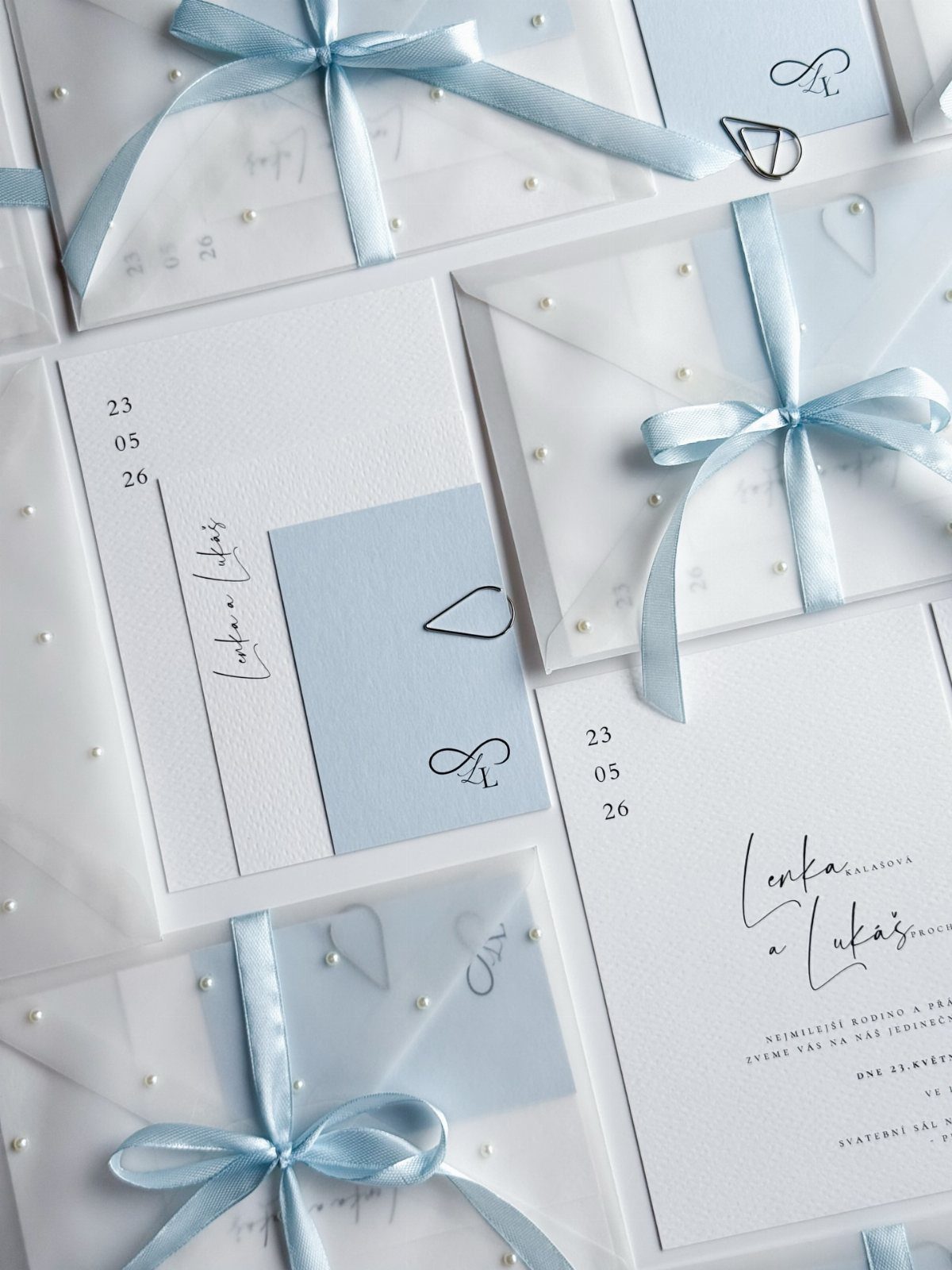 Light blue and white wedding invitations with satin ribbons and pearl accents.