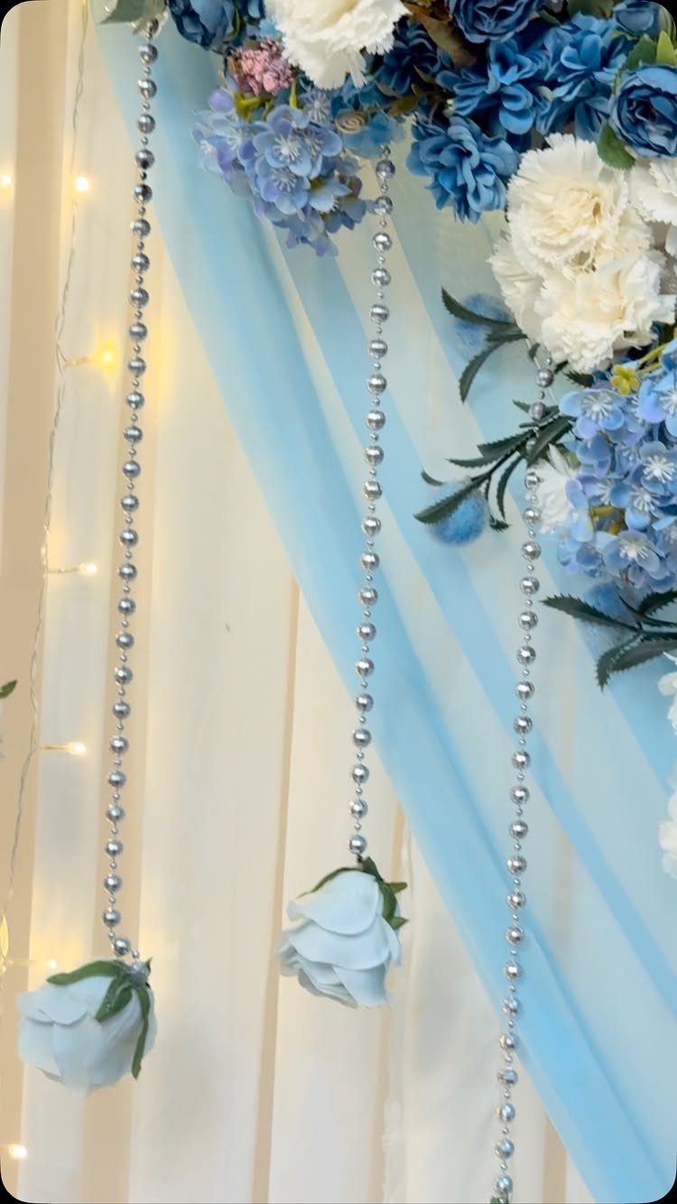 Light blue and white floral wedding backdrop with sheer fabric and silver bead curtains.