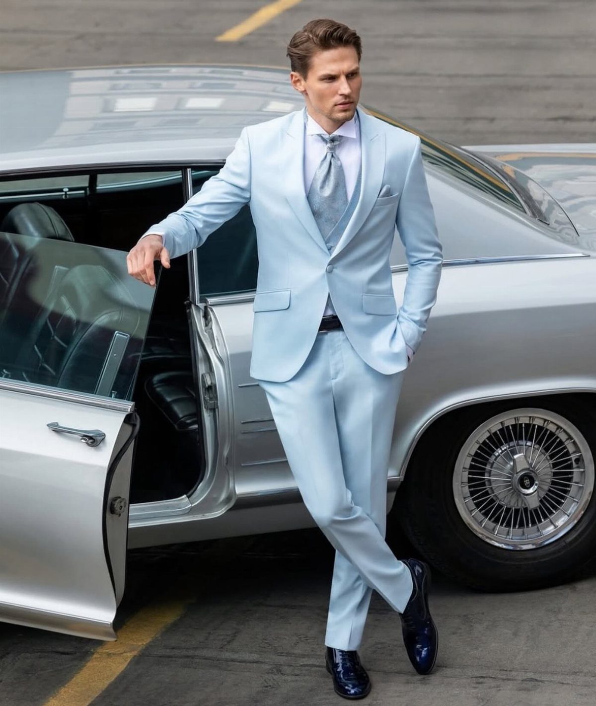 Man in a light blue suit leaning against a silver vintage car.