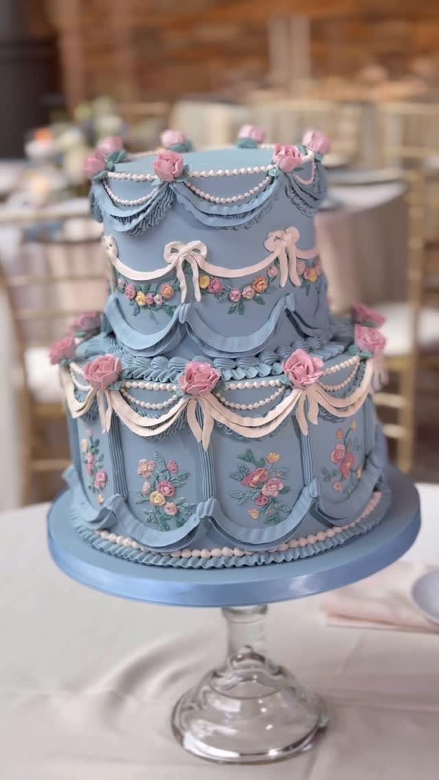Two-tier light blue wedding cake with pink roses and white pearl icing decorations.