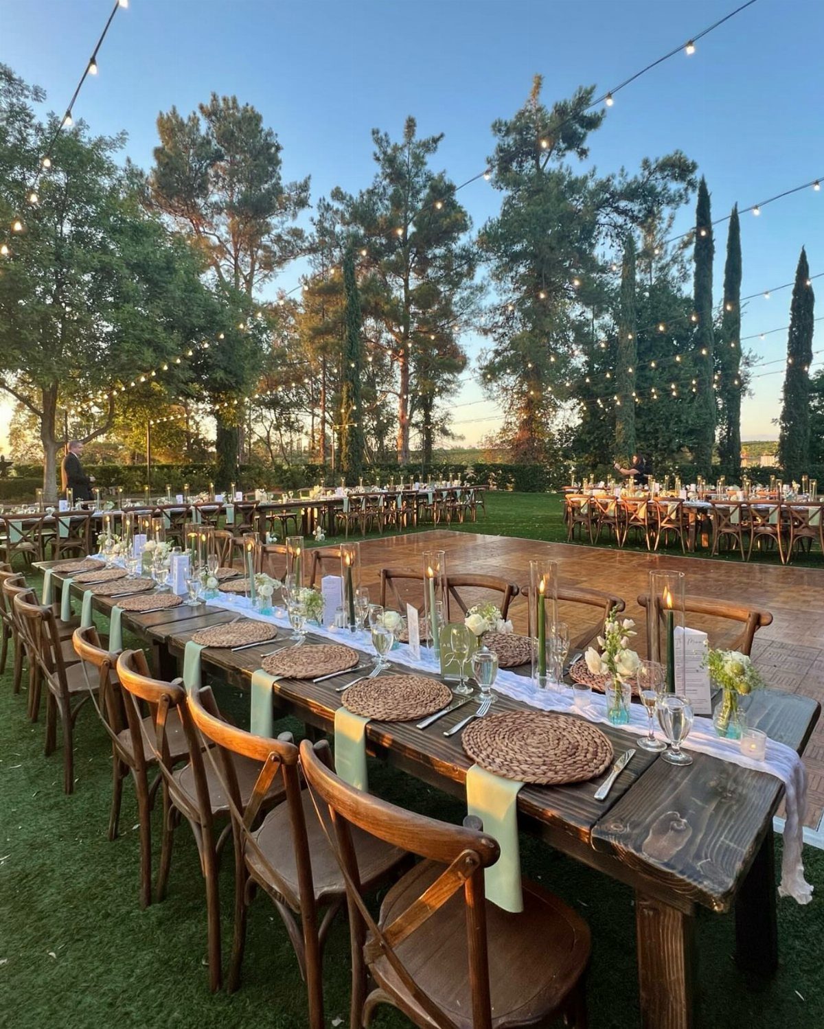 Rustic dark wood wedding table with woven placemats and chairs on a lawn