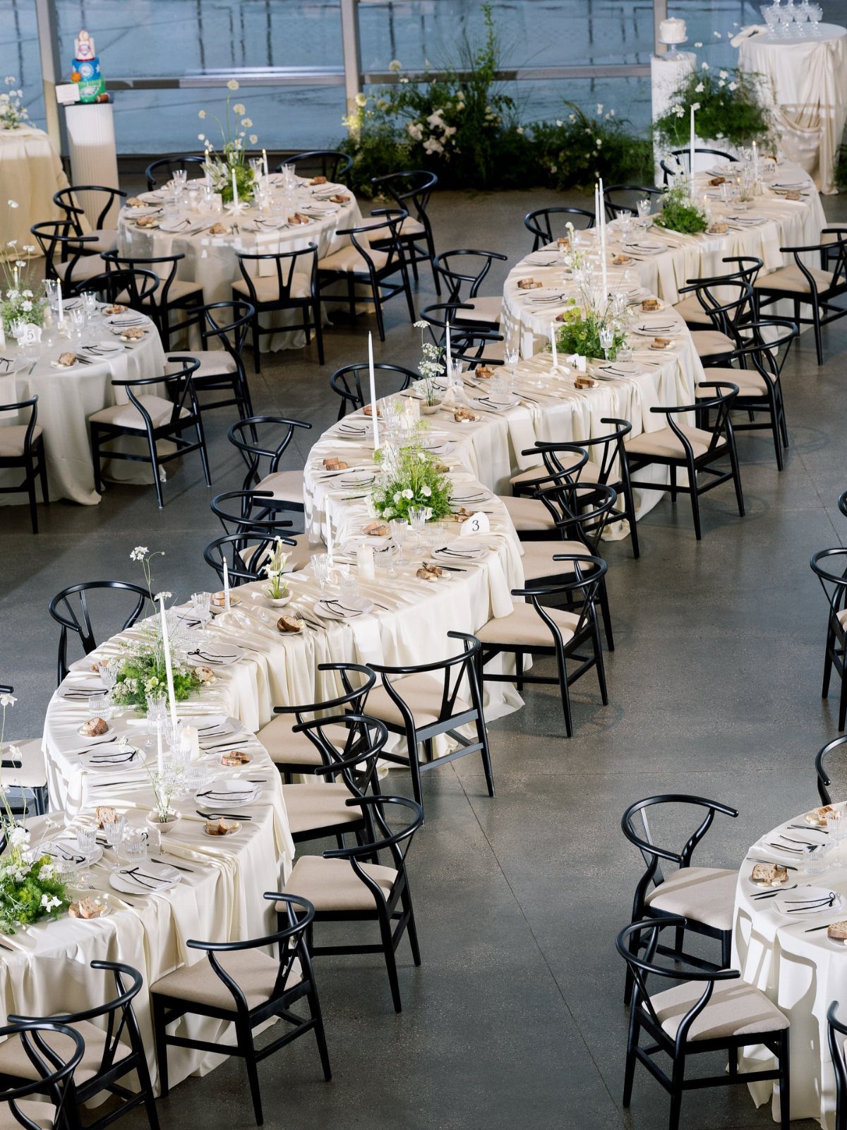 Curved serpentine wedding tables with cream linens, black chairs, and white floral centerpieces.