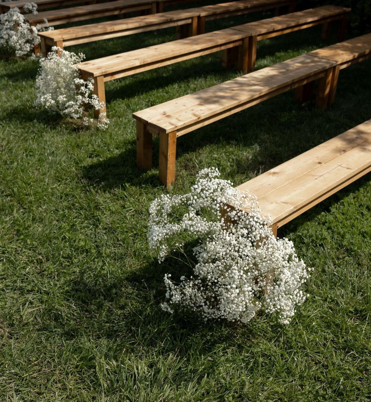 Wooden benches on green grass decorated with white baby's breath flowers for a wedding.