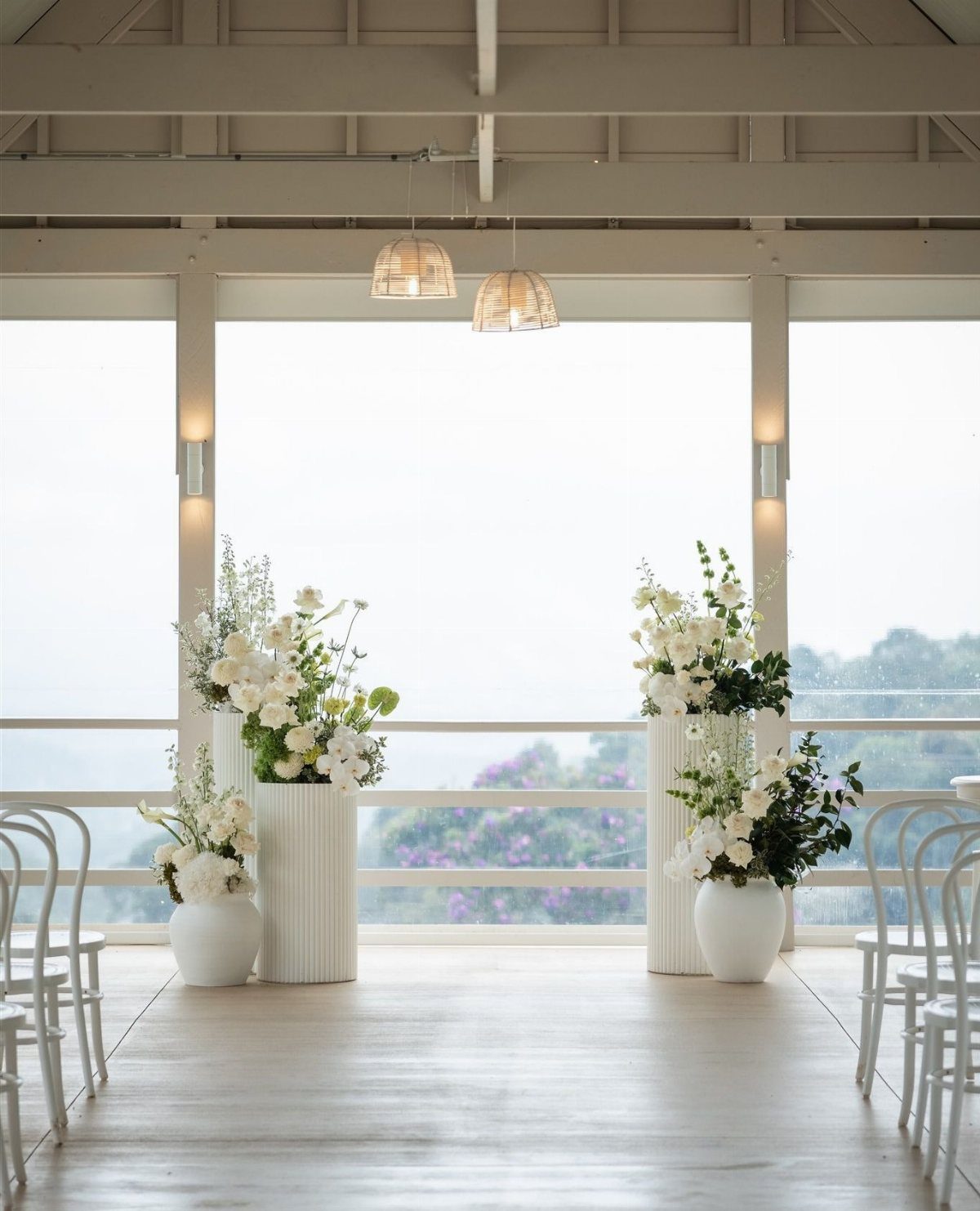 White floral arrangements on pedestals in a bright, minimalist wedding ceremony space.