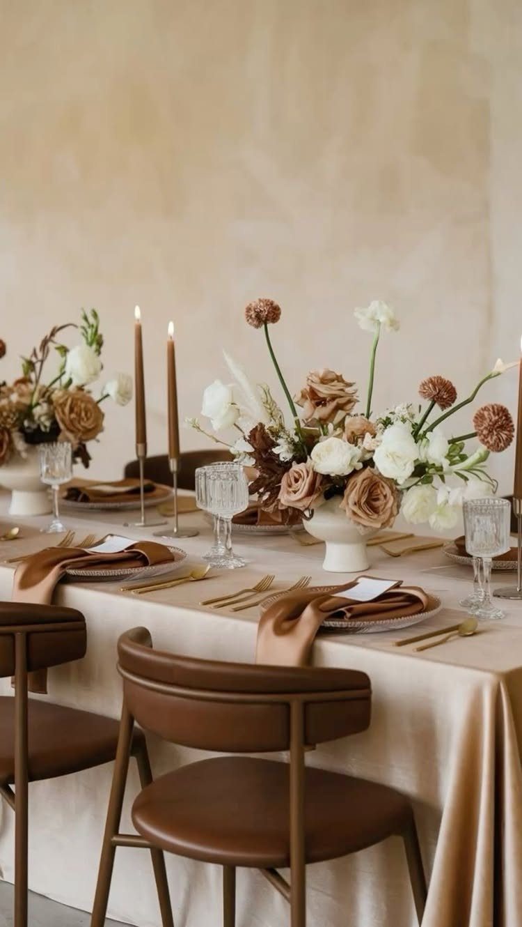 Wedding table setting with beige linens, brown leather chairs, and neutral floral arrangements.