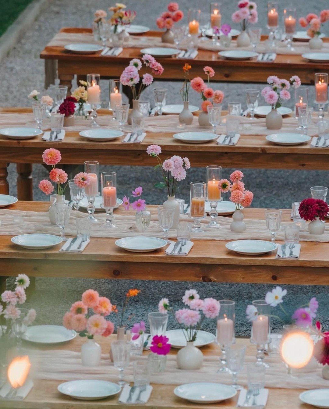 Wooden wedding tables decorated with muted blush flowers, white plates, and glowing candles.