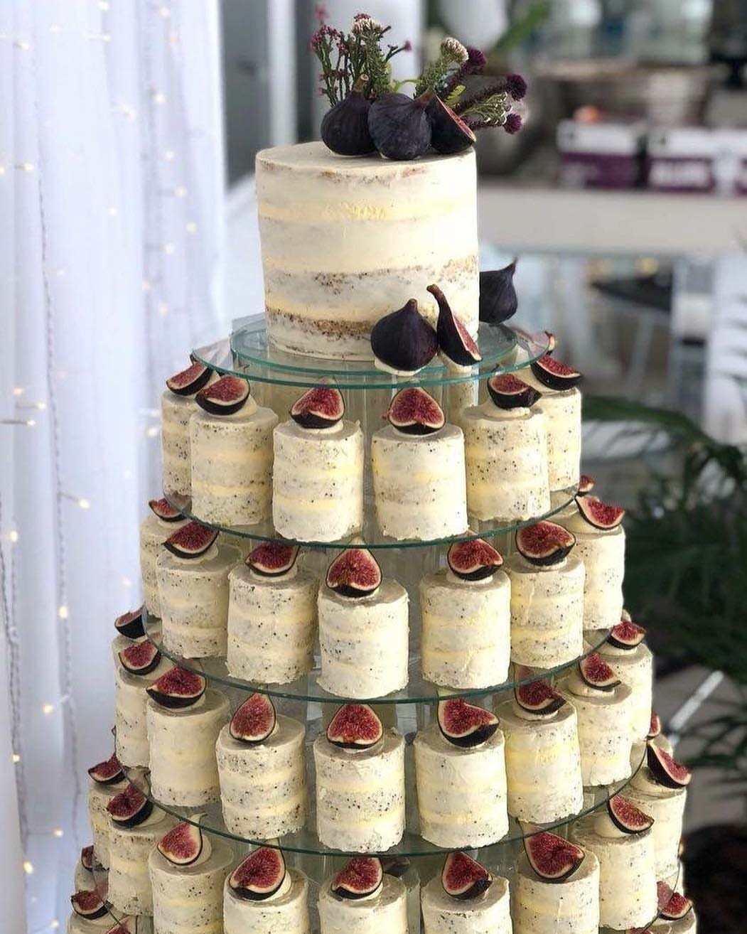 Semi-naked white wedding cakes topped with fresh figs on a tiered glass stand.