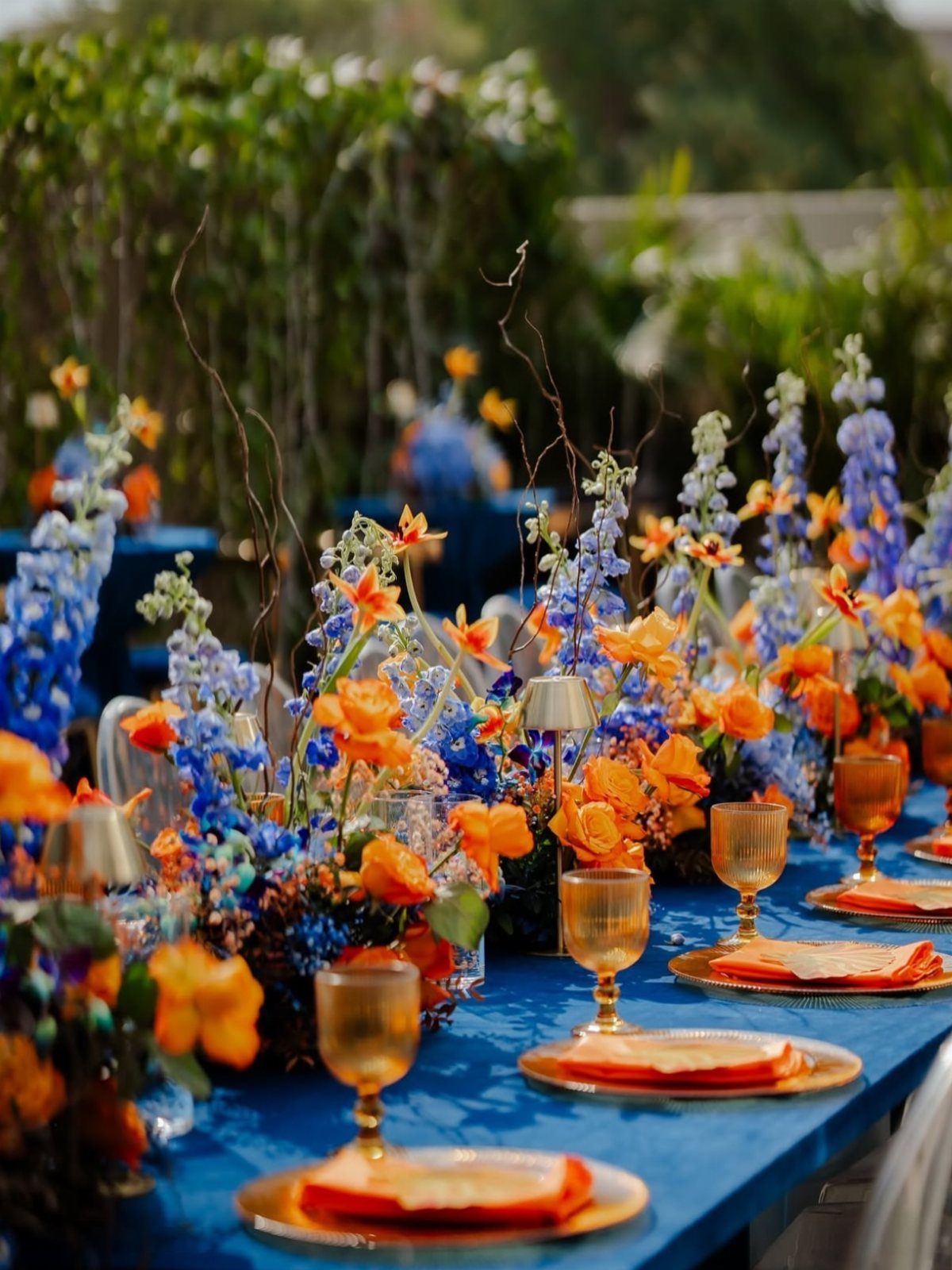 Navy blue table setting with vibrant orange flowers and amber glassware outdoors.