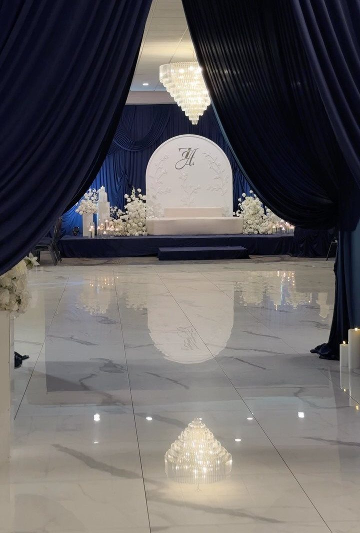 Navy blue curtains framing a white wedding stage with floral arrangements and marble flooring.