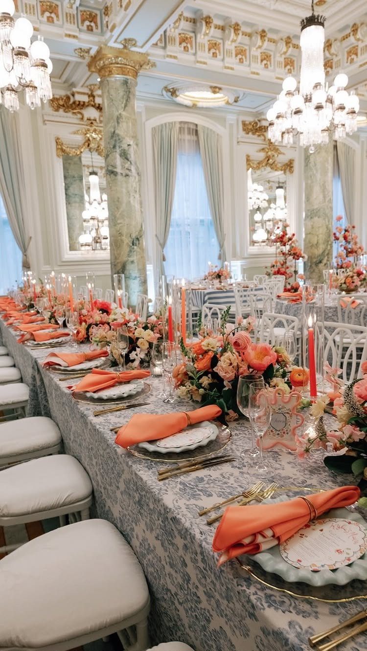 Long banquet table with salmon napkins and peach floral arrangements in a lavish room