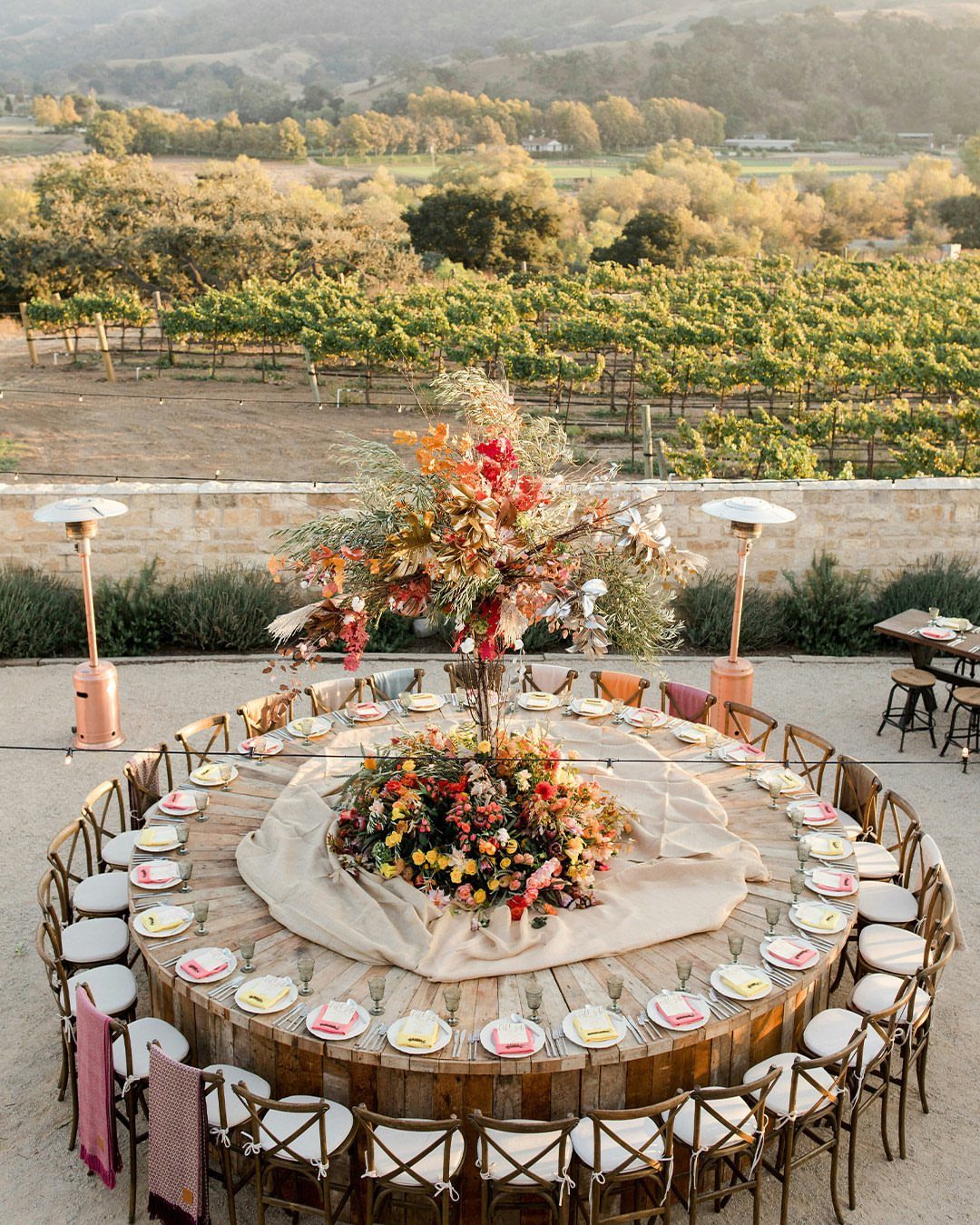 Circular wooden wedding table with red and yellow floral centerpieces overlooking a vineyard