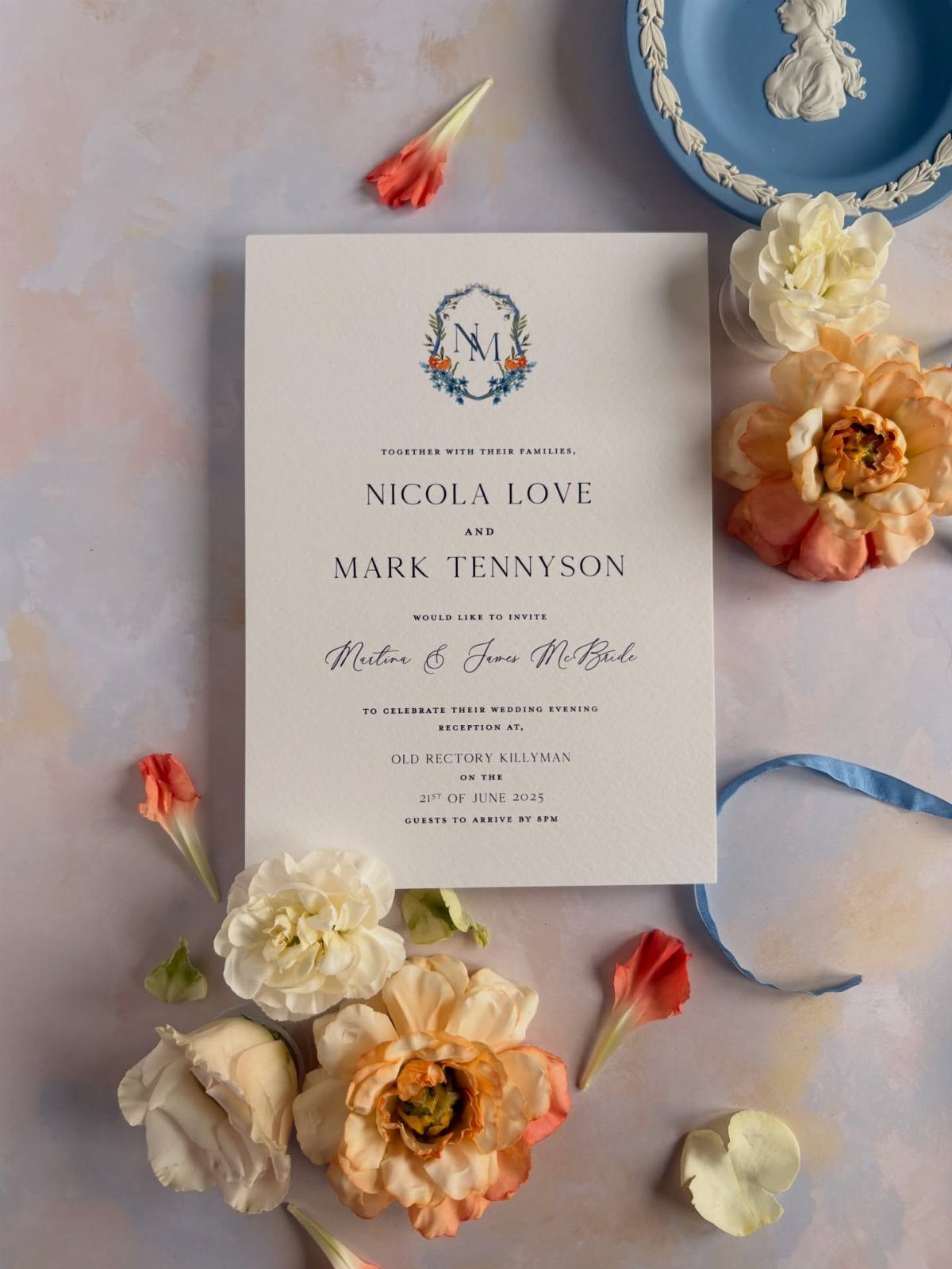 Wedding invitation with blue and orange floral details surrounded by fresh flowers.