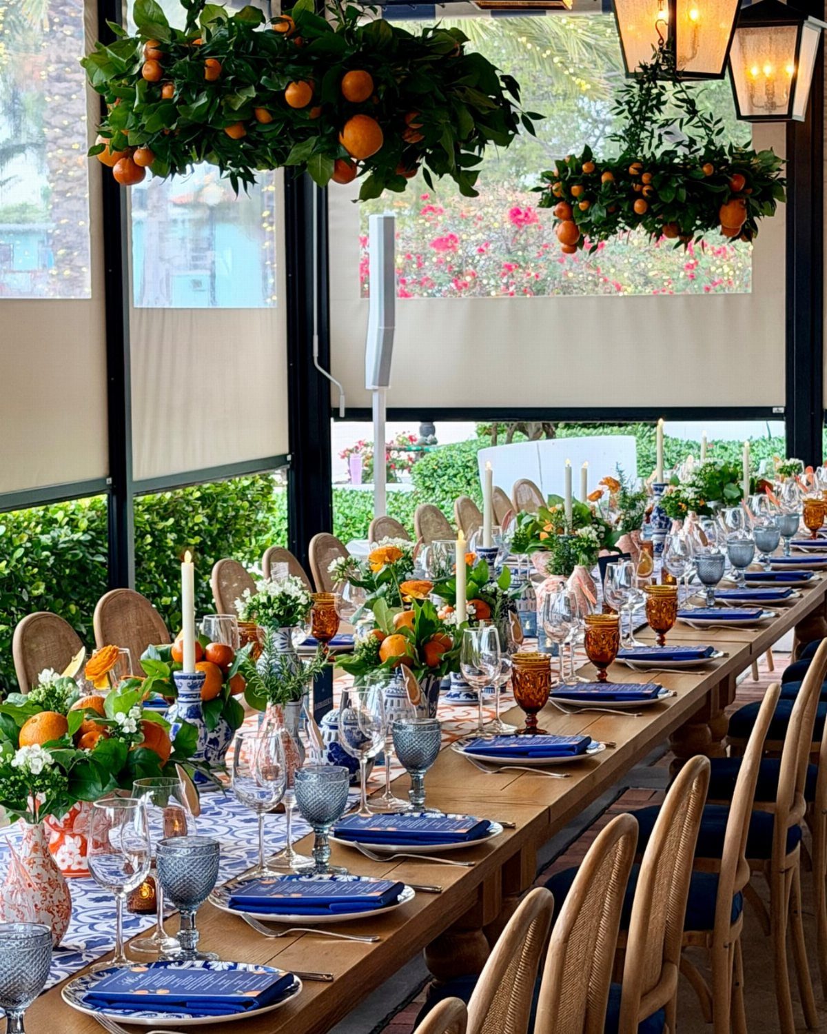 Long wooden table with blue dinnerware and orange citrus floral centerpieces.