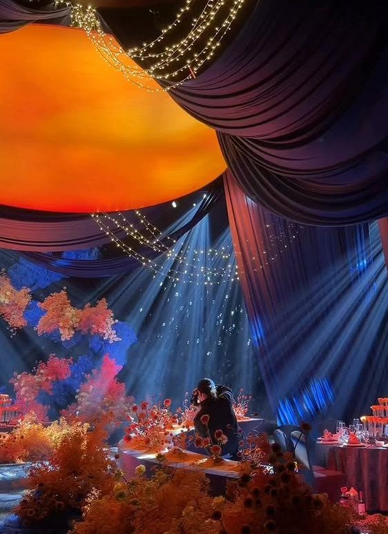 Event space with blue draping, orange ambient lighting, and orange floral arrangements.