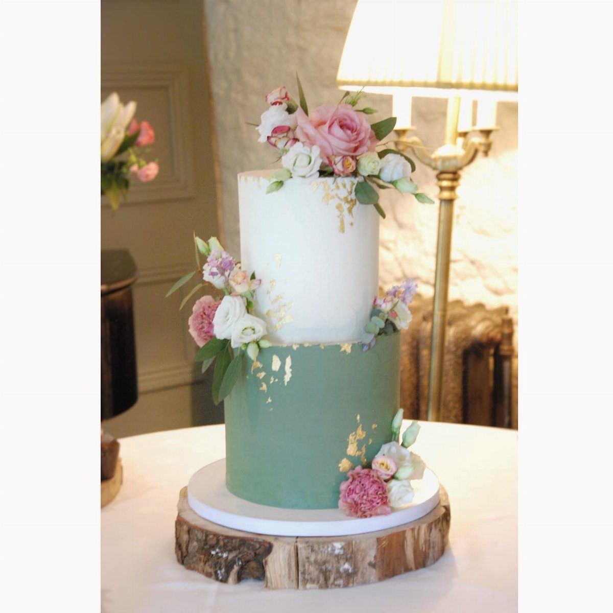 Two-tier wedding cake with white and sage green frosting, pink floral decorations.