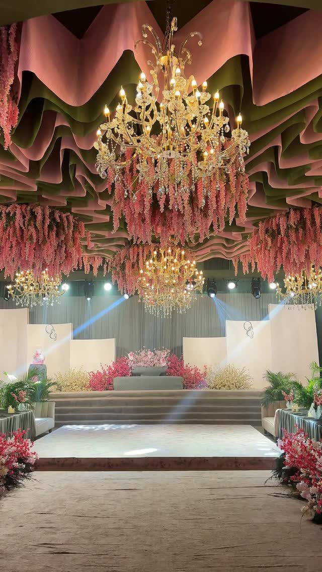 Ornate wedding venue with pink and green draped ceilings and crystal chandeliers.