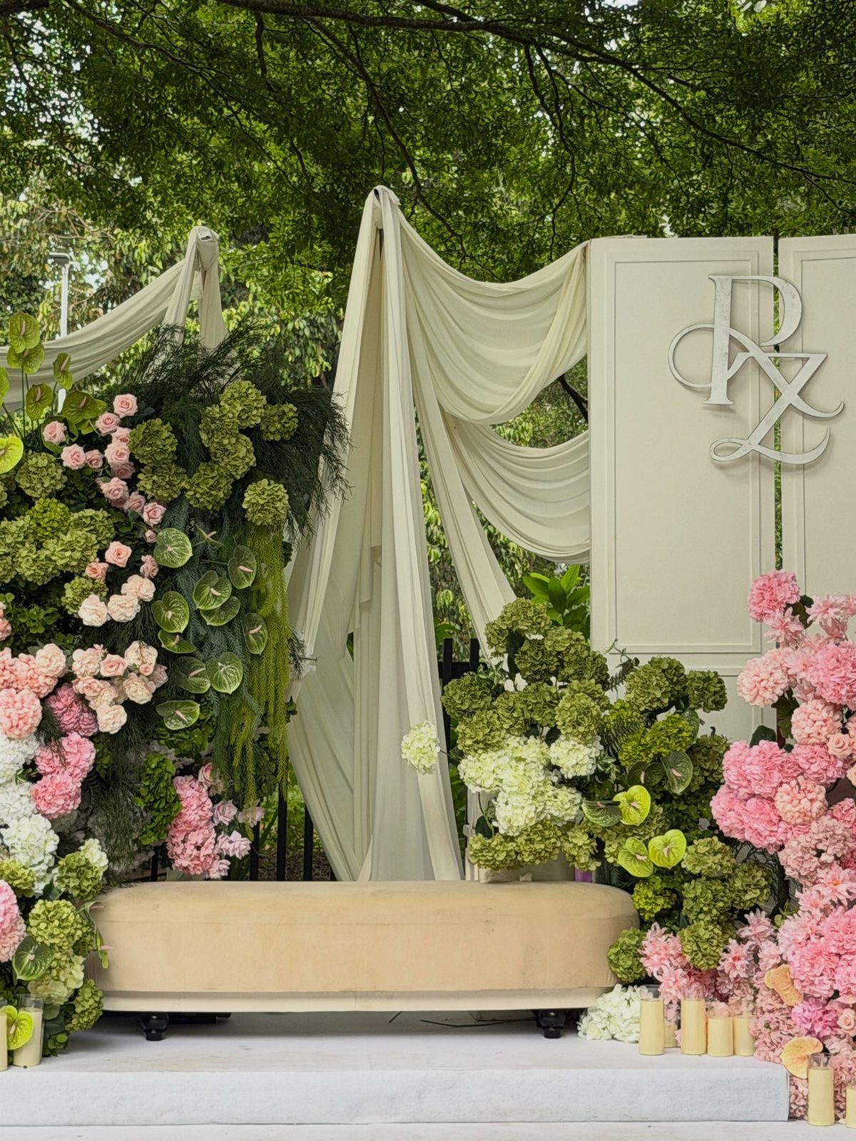 Wedding backdrop with cream drapes, pink and green flowers, and a beige bench.