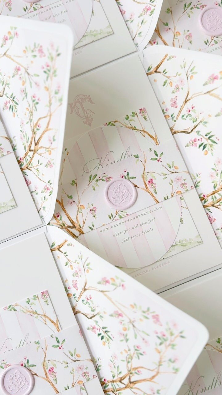 Wedding invitations with pink floral branches, green leaves, and pink wax seals.