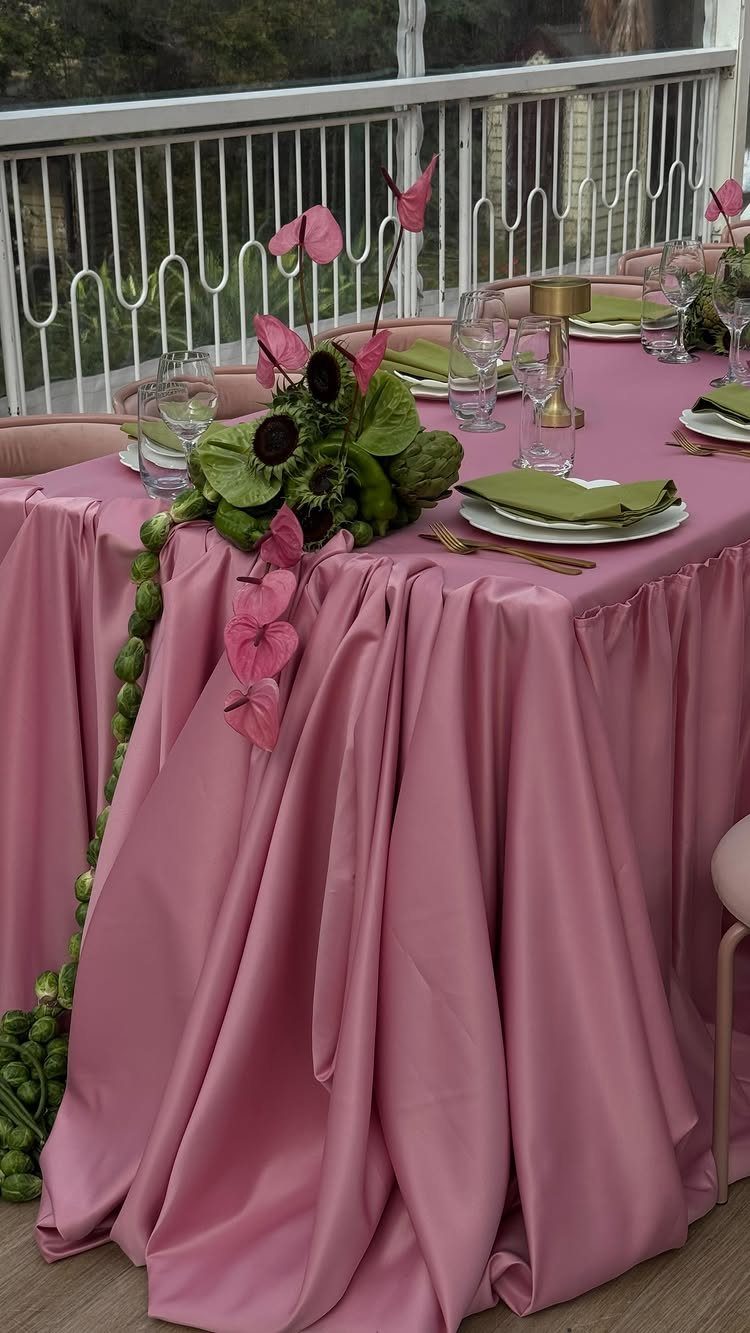 Pink satin draped table with green napkins and pink floral centerpieces on balcony