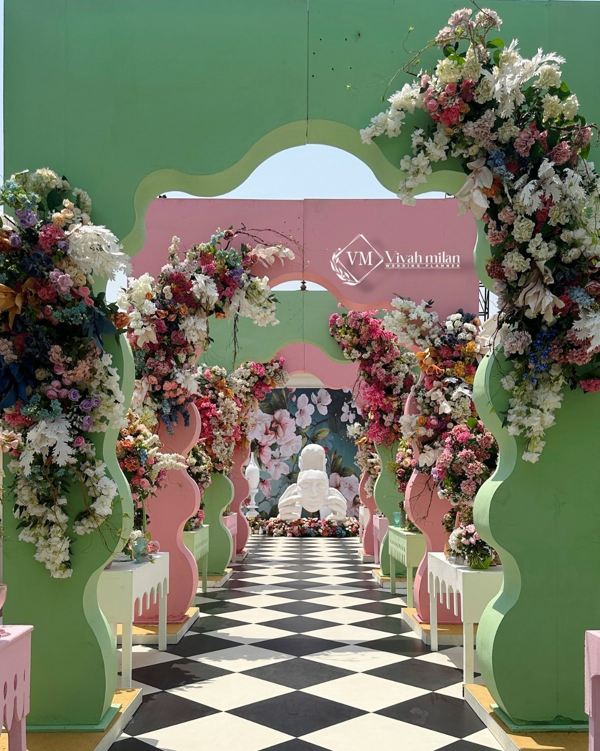 Green and pink scalloped arches with floral arrangements over a checkered floor.