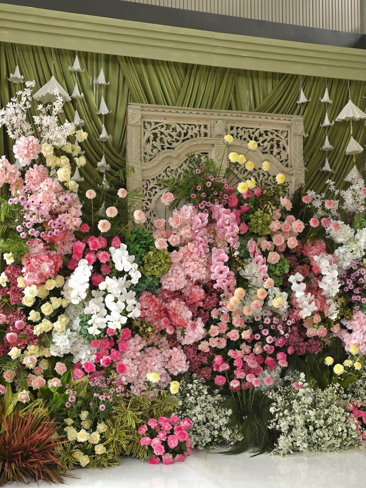 Floral wall with pink and white blossoms against olive green draped fabric.