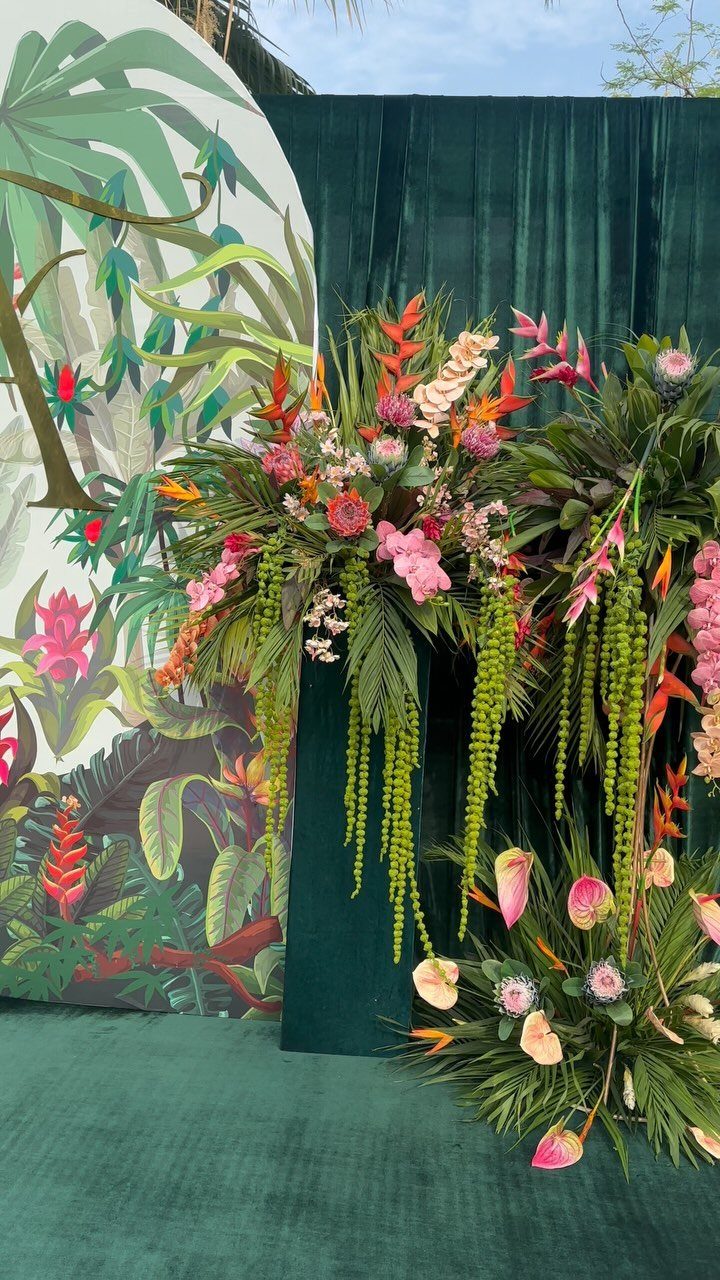 Tropical floral arrangements with pink flowers and green foliage against a velvet backdrop.