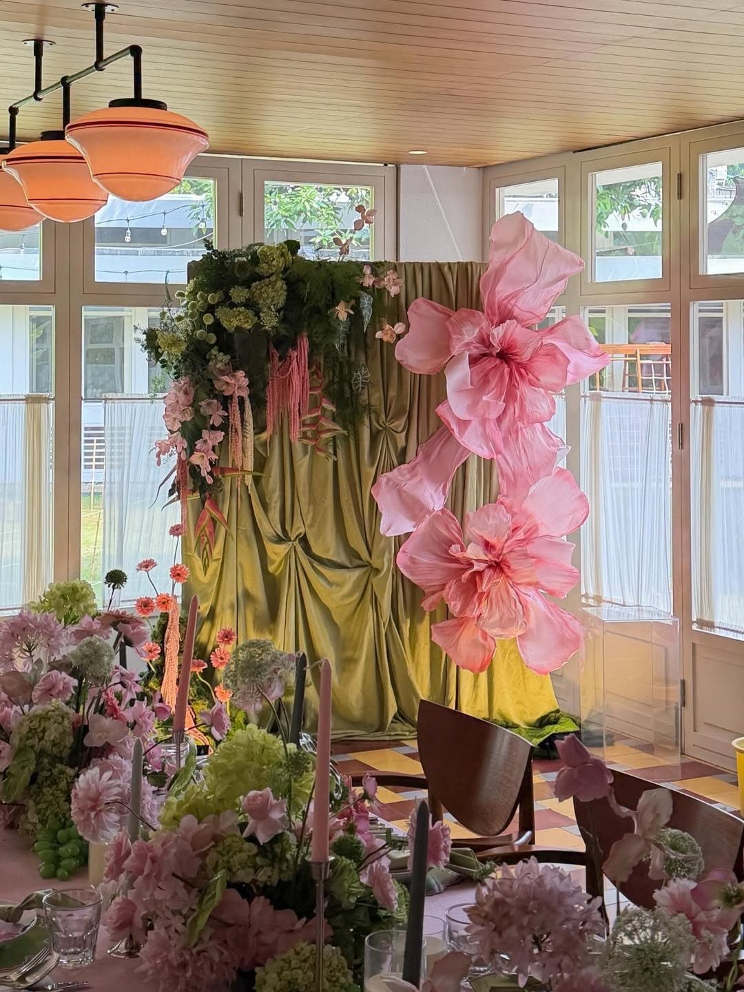 Gold satin backdrop with oversized pink paper flowers and lush pink and green florals.