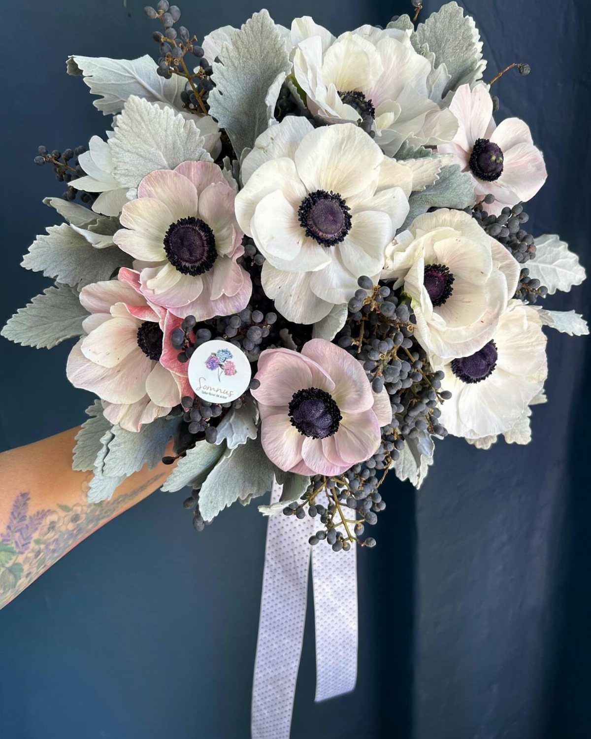 Bridal bouquet with white and pink anemones, silver foliage, and dark berries.